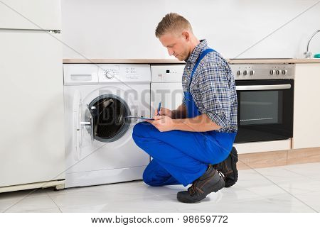 Repairman Writing On Clipboard In Kitchen