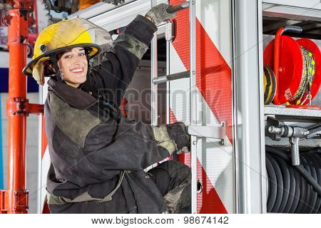Side view portrait of smiling female firefighter standing on truck at fire station