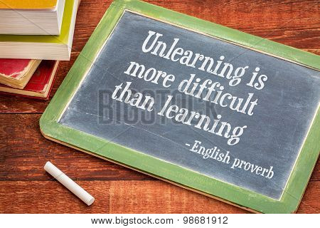 Unlearning is more difficult than learning - English proverb on a slate blackboard with a white chalk and a stack of books against rustic wooden table
