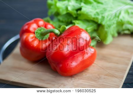 Vegetables lie on a chopping wooden board on a roustic table - salad and red sweet pepper. Close up photo