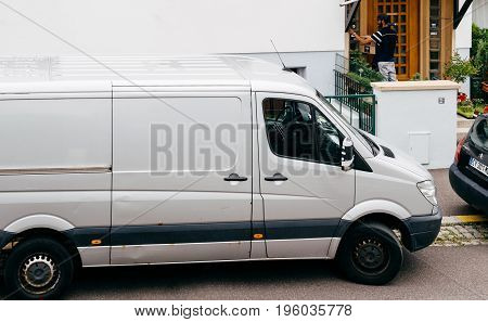PARIS FRANCE - JUL 12 2017: Young delivery man holding cardboard parcel box ringing at the doorbell and waiting the consignee to open the door and put the signature in clipboard