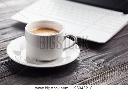Coffee cup and laptop on the wood texture selective focus on coffee cream.