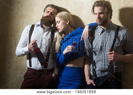 Girl sleeping with glass of liqueur and men with wine bottles. Friends relaxing with alcoholic drinks on beige wall. Alcohol and alcoholism. Friendship and convives. Unhealthy lifestyle and bad habits