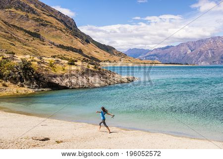 New Zealand travel happy tourist woman running of joy and freedom at beach shore of lake Hawea nature landscape. Near Wanaka, Otago Region