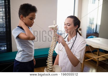 Female therapist pointing at artificial spine while explaining to boy in hospital ward