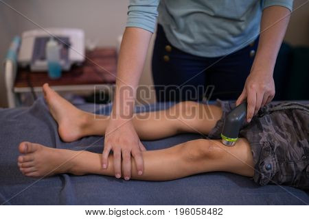 High angle view of female therapist using ultrasound machine on knee at hospital ward