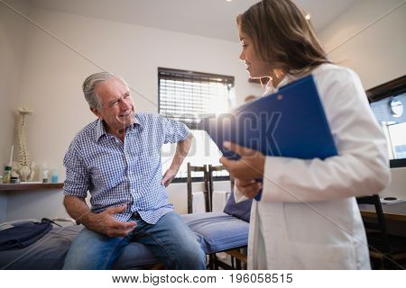Senior male patient showing back ache to female therapist with file at hospital ward