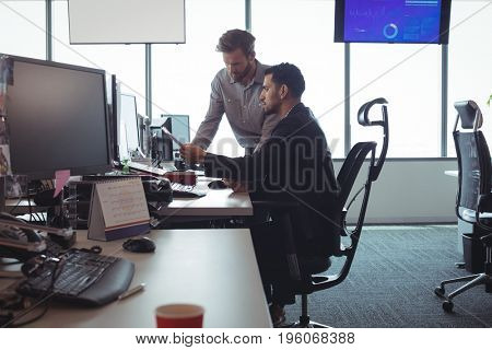 Male business colleagues discussing over documets at desk in office