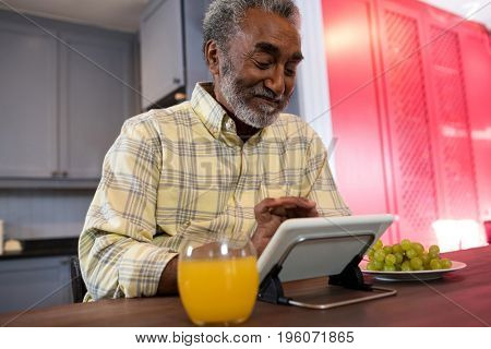 Happy senior man using tablet computer at table in kitchen
