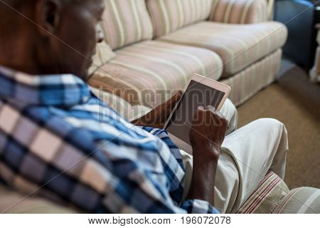 High angle view of senior man using tablet computer while sitting on sofa at home