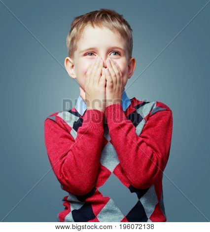 happy excited child cllosing his face and wearing a sweater  isolated against grey background