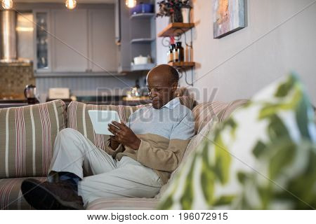 Senior man using tablet computer while sitting on sofa in living room at home
