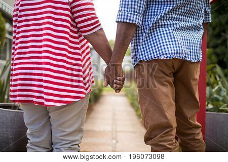 Midsection of couple holding hands while standing in yard