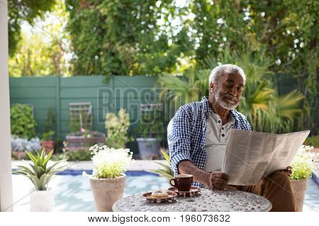 Senior man reading newspaper while sitting at table in yard