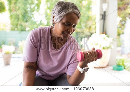 Close up of senior woman exercising with dumbbell while sitting in yard