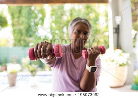 Portrait of senior smiling woman exercising with dumbbell while sitting in yard