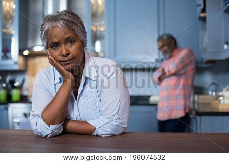 Woman with hand on chin leaning on table in kitchen