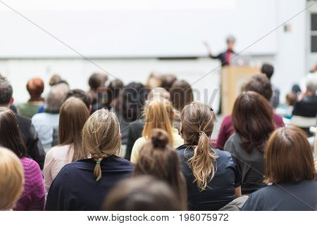 Female speaker giving presentation in lecture hall at university workshop. Audience in conference hall. Rear view of unrecognized participant in audience. Scientific conference event.