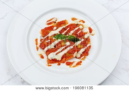 Ravioli with tomato sauce served in white plate on marble serface.