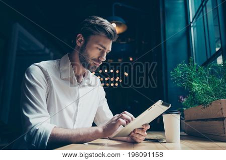Side View Of A Young Sexy Entrepreneur, Browsing On His Tablet In A Dark Designed Modern Cafe, Well