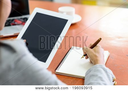 Beautiful Asian businesswoman was looking at the tablet and taking notes on her desk on the wood table in her office. Finance Banking and Technology Concepts.