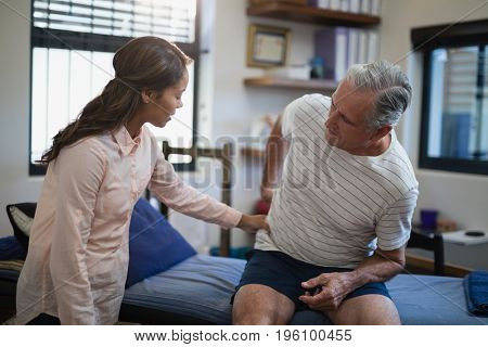 Female therapist examining back of male patient sitting on bed at hospital ward