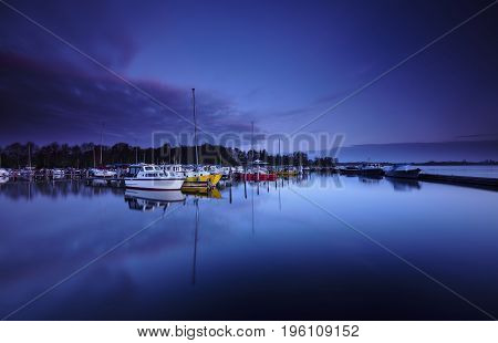 Small and colorful yachts at a platform reflected in a calm lake under a blue dawn