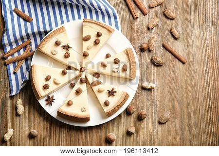 Delicious sliced cheesecake with nuts on wooden table