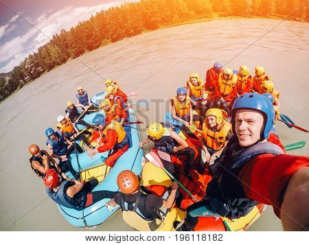 mountain Altai, RUSSIA - July 16, 2017: man in a helmet holds an action camera and makes selfie on the background of friends with oars, rafting