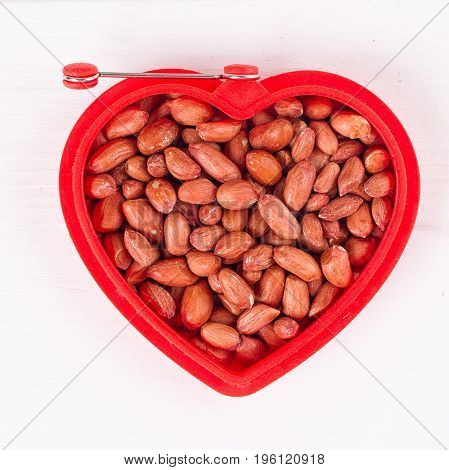 Raw peanuts in heart bowl on the white background