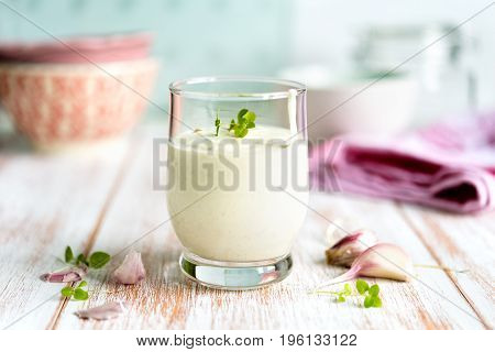 Close up of a homemade garlic sauce in a glass with garlic gloves arranged on rustic wooden table