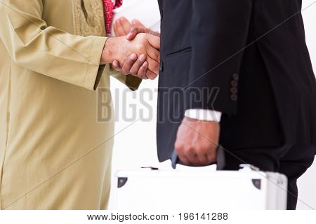 Arab business man shake hand with Asian business man in the blakc suit carrying a silver suit case.