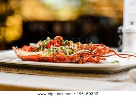 Italian cuisine. Whole lobster baked and sliced in half Served with tomato salad and sauce on white plate on marble serface.