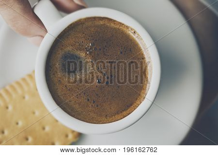 Closeup of tasty coffee espresso with tasty foam in small ceramic cup. Female hands holding warm hot drink.