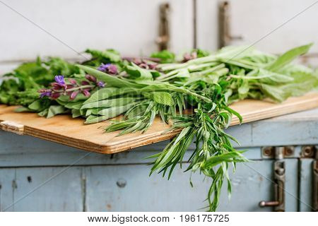 Assortment of fresh herbs mint, oregano, thym, blooming sage on cutting board over old blue white wooden kitchen table. Rustic style, day light.