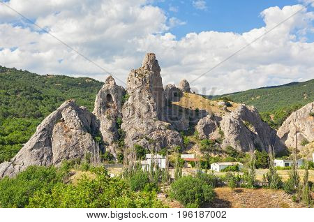 The mountain is an unusual form with a grotto in the background of hills with forests and a cloudy sky. Delikli-Kaya rock peninsula of Crimea