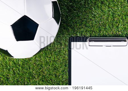 The ball for playing football lies on a green lawn as a background and there is a place for recording the result