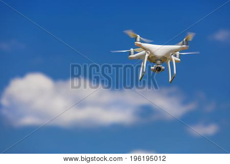 Professional camera drone flying in clear blue sky partly clouded.