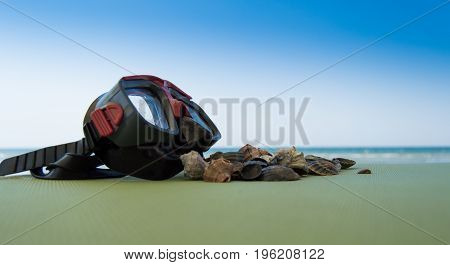 mask scuba dive with sea shells on the sea coast. blue green background.