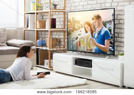 Young Woman Lying On Carpet Enjoying Watching Television At Home