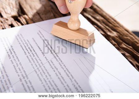 Person Holding Stamp On Document Over Wooden Desk