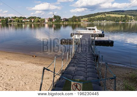 A barrel jet leading to the boat. Background view on village Frymburk Lipno lake Czech Republic. Frymburk in sunny day view from Frydava port.