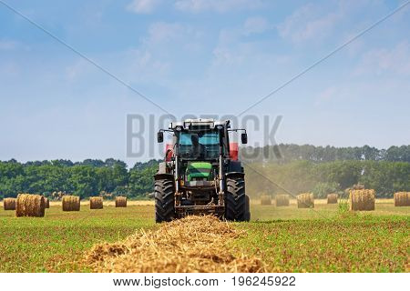 Tractor in a farmer field with balls of straw.