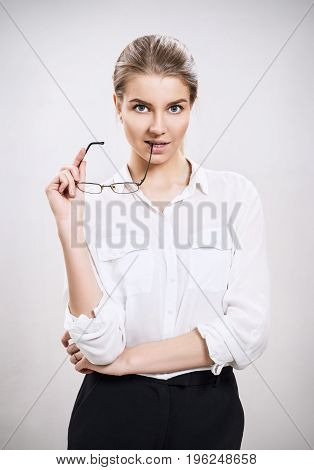 Attractive businesswoman holds glasses in hands over gray background.