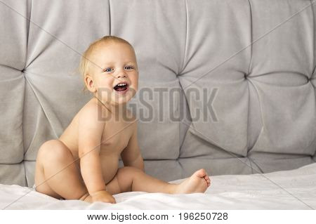 Adorable smling toddler sitting on the bed against the grey background. Copy space.