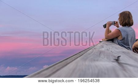 A woman with a mobile in her hand is photographing the surrounding landscape. at the top of the observation tower and watch the surroundings. Treetop Walkway in Lipno.