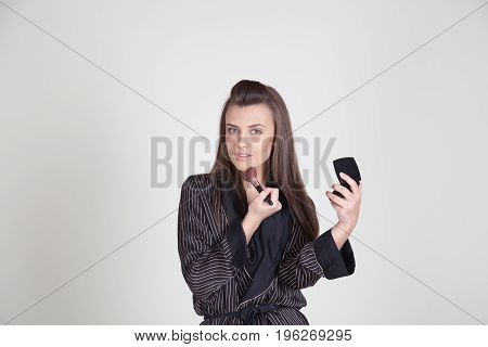 girl in coat makes brush makeup looks in the mirror 1