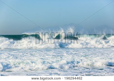 Waves swells crashing ocean water power towards beach coastline.