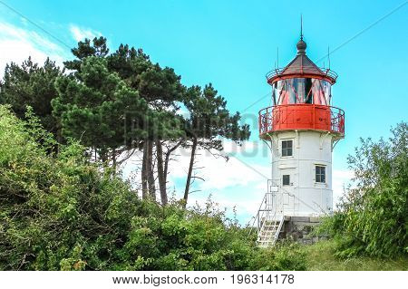 Vintage lighthouse Gellen on a wooded dune between trees and bushes. Sunny summer day. Nice blue sky with clouds in background. Hiddensee, Germany. Baltic Sea