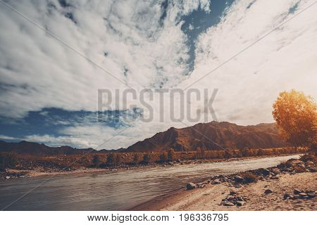 Wide angle view of Katun mountain river on morning with mountains and hills in background dark blue sky with cloudscape birch and stony shore on the right Altai Kuyus district Russia